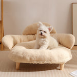 Cream bouclé XL pet couch bed with wooden legs and raised sides holding a small white fluffy dog on a beige rug
