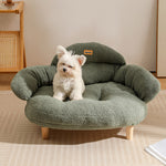Small fluffy white dog sitting on a green bouclé XL pet couch bed with wooden legs in a bright room