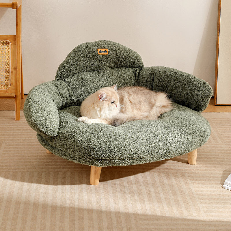 Fluffy light-colored cat resting on a green bouclé XL pet couch bed with wooden legs in a living room