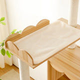 A tall and sturdy LOLOPAWS cat furniture tower with wooden cat shelf with a cushion on a wooden floor, next to a plant.